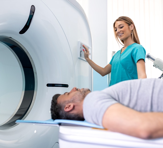 Female nurse helping to send male patient through CT scan