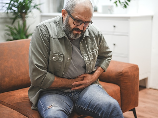 Male sitting on couch holding stomach in pain from a hernia