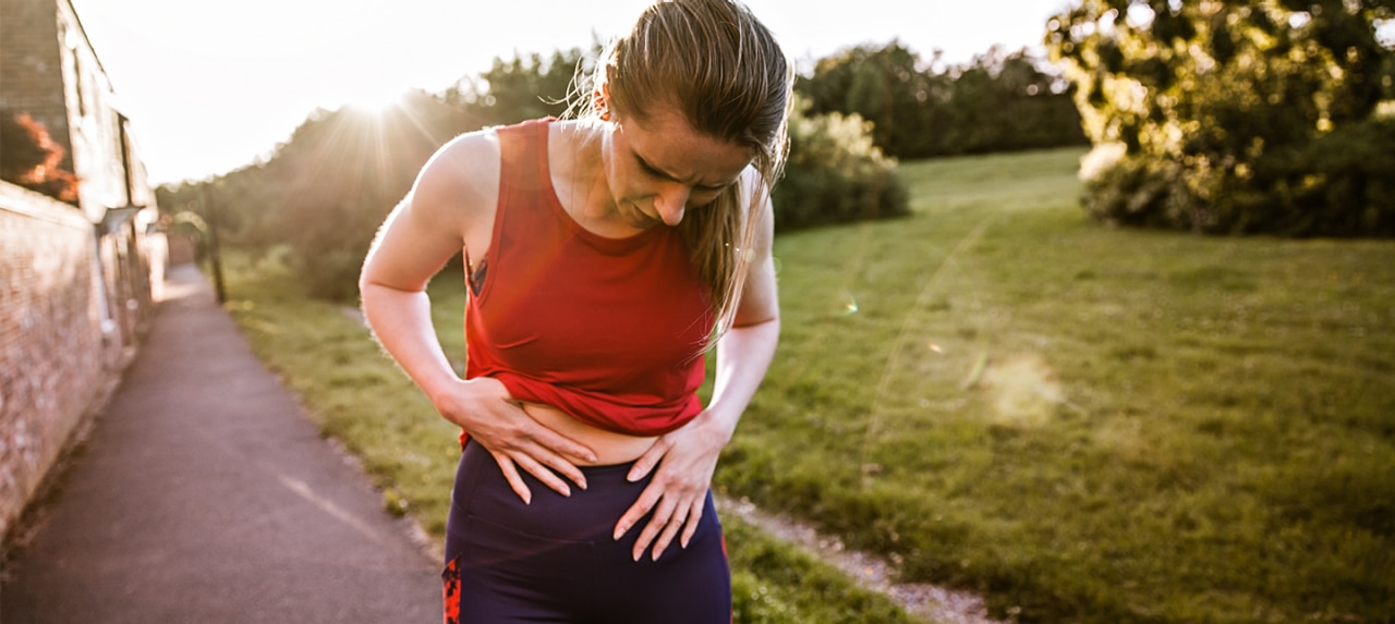 Woman in workout gear holding her abdomen in pain