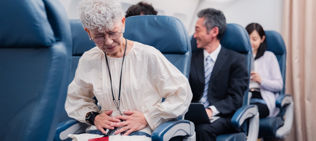 Elderly woman sitting in plane seat having abdominal pain