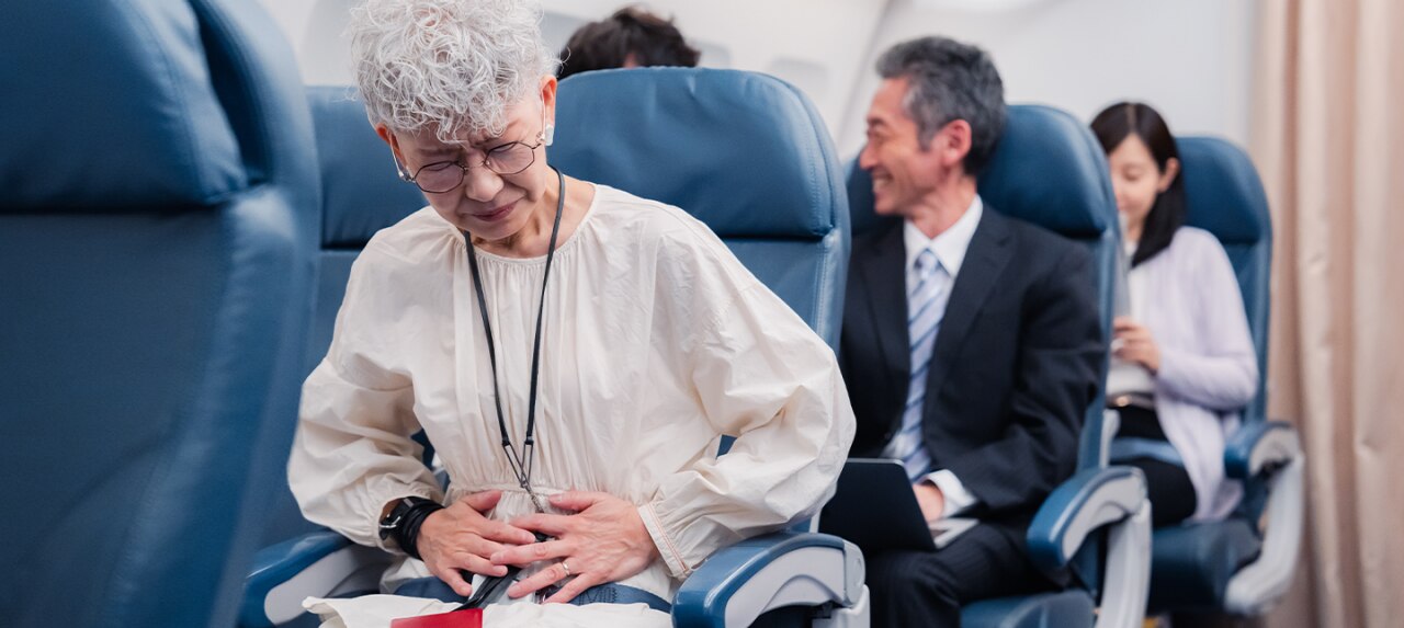 Elderly woman sitting in plane seat having abdominal pain